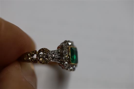 An antique 18ct gold, emerald and diamond cluster ring, the central square cut emerald (0.88ct) bordered by 14 old cut diamonds,
